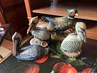 Four ceramic bird figurines including mallard and pelicans, arranged on a table with wooden cabinet background