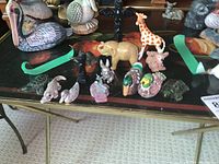 Top down and front angle of 14 small figurines including animals and 2 totem poles on a glass table.