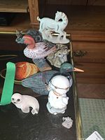 Photos show ten figurines including animals and an angel, arranged on a reflective glass surface with wooden drawers in the background.