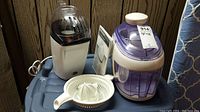 Two kitchen appliances on a blue storage bin; juice extractor with strainer and manual, electric popcorn maker with purple lid.