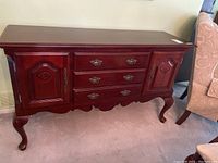 Full front view of cherrywood sideboard showing three drawers in center and a door on each side, standing on carved legs.