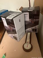 Two boxed Canvas solar lights and a round wooden framed thermometer on beige surface