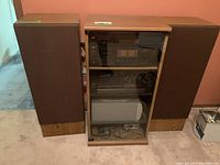 Front view of the stereo cabinet with two large speakers on each side; shows the receiver and components inside glass door.