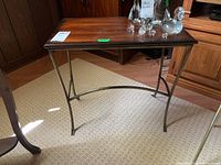 Side view showing the metal legs and wooden top of the small side table on a carpeted floor.