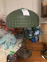 Front view showing green glass dome shade with geometric relief pattern and bronze-tone base