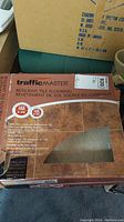 Box of TrafficMaster vinyl tile flooring showing brand name and product type with window displaying tile pattern