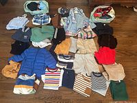 Overview of children's clothing lot including multiple shirts, shorts, jackets, and hats.