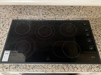 Top-down view of black ceramic glass cooktop showing five heating zones and side-mounted knobs