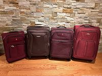 Front view of four luggage pieces arranged side by side against stone wall backdrop on wood floor.