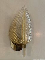 Front view of sconce showing leaf-shaped glass shade mounted on round brass backplate