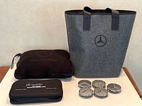 Mercedes-Benz first aid kit, blanket, felt bag, and set of 5 chrome wheel center caps displayed on table.