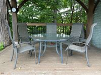 Photo showing hexagonal glass top table with 4 chairs around it on wooden deck.
