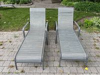 Front view of two gray metal frame lounge chairs with sling seats on a brick patio