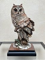 Full front view of the owl figurine showing detailed feathers, perched on tree stump base with foliage and rocks.