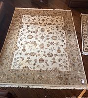 Full top-down view of hand knotted area rug measuring approximately 10ft by 8ft showing central floral medallion pattern on cream field with beige and brown border