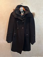Front view of a black wool winter coat with double-breasted buttons and coyote fur trimmed hood.