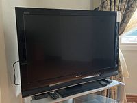 Front view of the Sony Bravia TV showing the screen, frame, and stand with remote control on platform below.