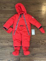 Full view of the red Canada Goose toddler snowsuit laid flat, showing hood, mittens, and booties.