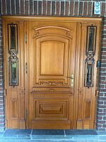 Front view of the solid wood exterior door with decorative carved panels flanked by two double transom windows with wrought iron grills.