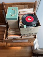 Three cardboard carriers and a turquoise music-note box filled with paper-sleeved 45s on a wood chair