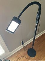 Five different adjustable floor lamps with black flexible gooseneck necks and rectangular LED panels or lamp heads placed on a wood floor near a beige wall.