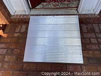 Top view of flat aluminum ramp placed against threshold on brick surface showing ribbed pattern