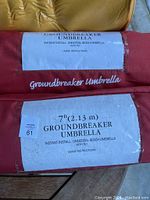 Close-up image of two GroundBreaker umbrella sleeves labeled 'Instant Install Universal Beach Umbrella' with length 7ft (2.13m).