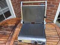 Front view showing open grill press with grooved bottom and flat top plates, control panel with knob and switch visible.