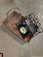 Photo showing two wire baskets, one silver two-tier with handle, one black decorative basket containing sunflower tiled bowl