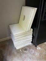Stack of approximately 40 white drop ceiling tiles, some with circular holes for lighting, showing light wear and stains.