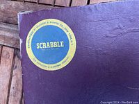 Close-up of the Scrabble game box showing the label with the manufacturer's name Selchow & Righter Co, New York, and the Scrabble game name.