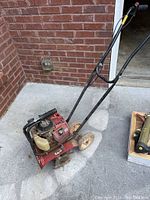 Side view of the red Honda tiller with mounted black handle and wheels.