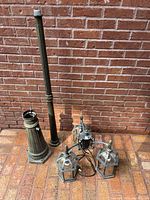 Full view of lamp post parts on brick floor including base, pole and triple lantern fixture with wiring.