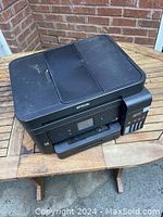 Full view of black Epson EcoTank printer on wooden table against brick wall