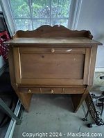 Front view of the wooden drop-leaf secretary desk showing the decorative scalloped top back panel and closed fold-down front panel.