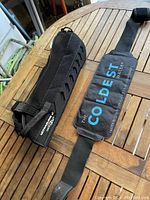 Photo showing black shoulder sling with attached cooling pack labeled 'THE COLDEST WATER' laid on wooden table.