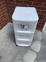 White plastic three-drawer storage cabinet placed outdoors against a brick wall showcasing overall condition and design.