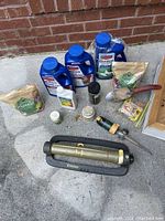 Photo showing three large blue bottles labeled as plant feed, two bags of granular fertilizer, a small white bottle, a black shaker, pellet container, metal oscillating sprinkler, brass spike sprinkler, and garden trowel.