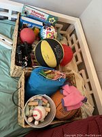 Two wicker baskets filled with assorted toys including small balls, wooden pieces, and a children's book.
