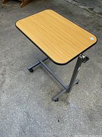View of adjustable TV table showing wood grain laminate top, black edge trim, metal base with castors and adjustable height knob.