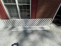 Long white vinyl lattice panel outdoors laying against wall with ground shadows
