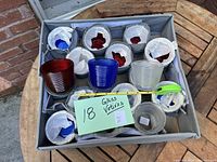 Photo showing 18 glass votive candle holders in red, white, and blue in a gray cardboard carrying box on wooden surface with measuring tape.