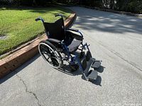Manual wheelchair showing side angle, highlighting cushioned seat, backrest, large rear wheels, and footrests.