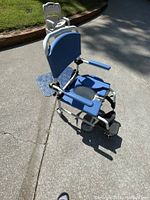 Side view of blue padded medical transport wheelchair with white frame, armrests, and footrests, showing seat cut-out and wheels