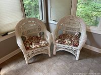 Two white wicker chairs side by side with floral cushions
