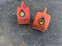 Two orange plastic gas tanks on ground, one missing top cap, both with round openings and handles.