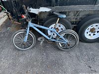 BMX bike leaning against trailer showing full side profile including frame, tires, seat, pedals, and handlebars.