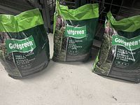 Three green and black bags of Golfgreen Tree & Hedge Feeder fertilizer on a concrete floor, showing the front of the packaging.