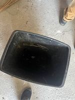 Top view inside the black plastic garbage bin, showing empty interior with some dust and minor debris.