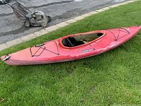 Full side view of red kayak on grass with lawn mower in background